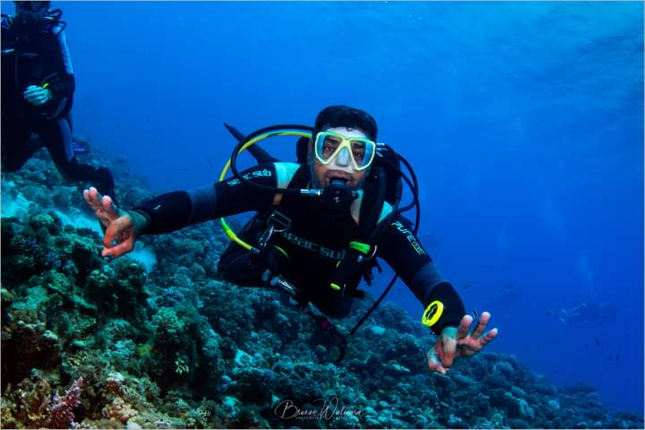 Osama swimming over coral reef in Scuba Sub gear with yellow mask, giving OK sign, professional underwater photo by Bruno Walmora