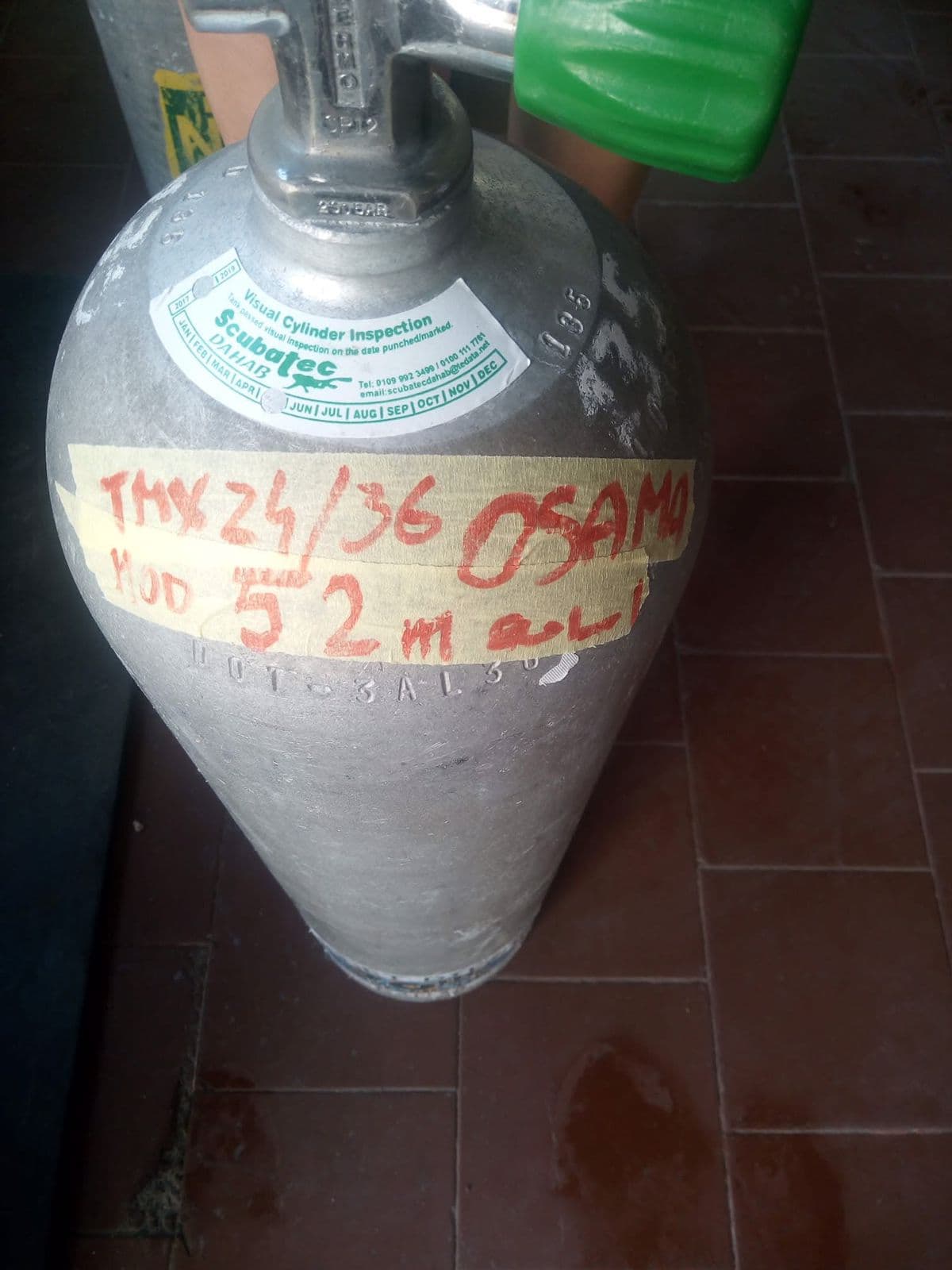 Close-up of a gray aluminum trimix tank with red marker text reading TMX 24/36 OSAMA MOD 52m, ScubaTec Dahab visual inspection sticker, green valve handle