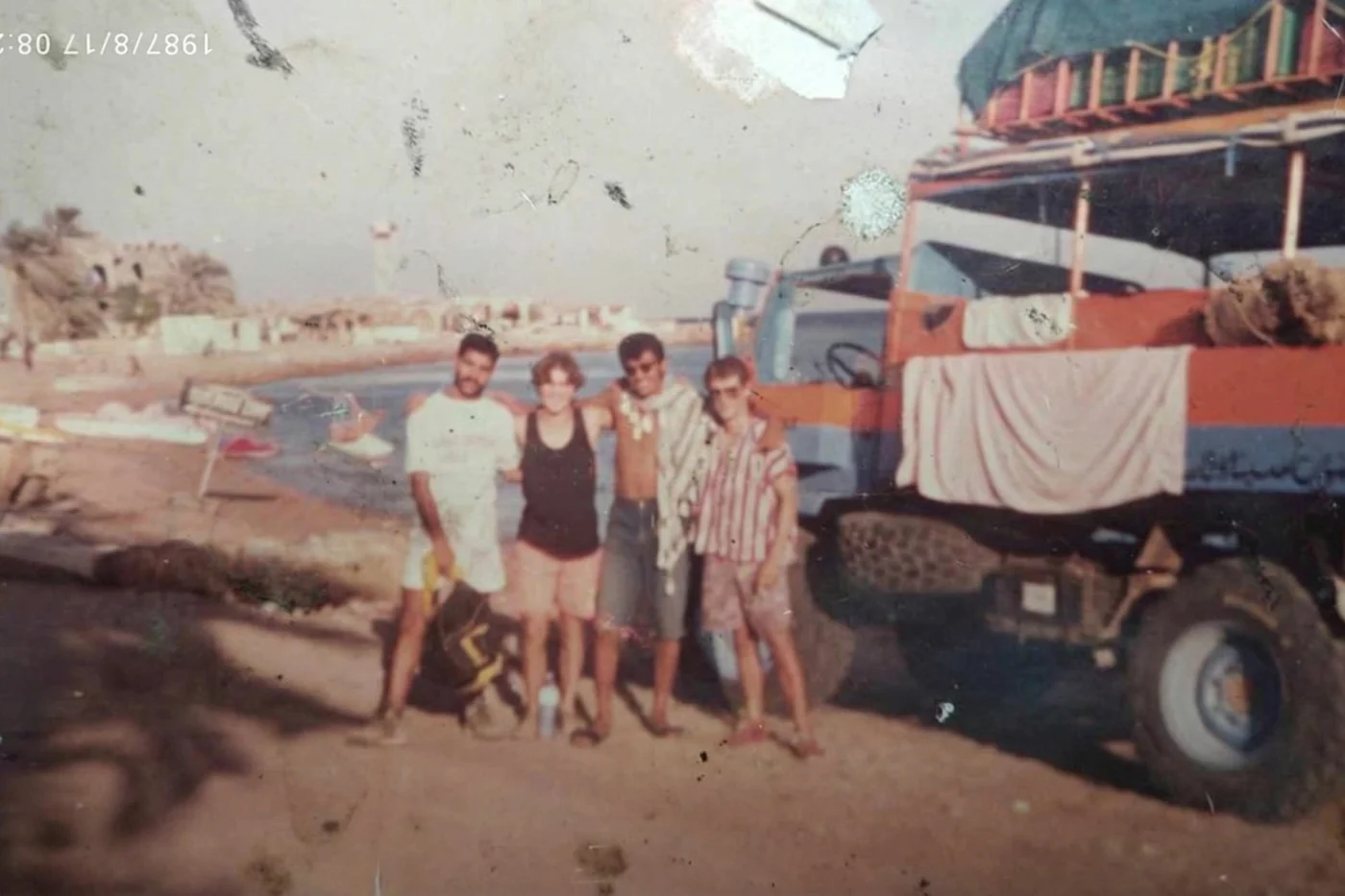 The original scratched August 1987 photograph: four young people beside an orange Bedouin truck on the Dahab shore