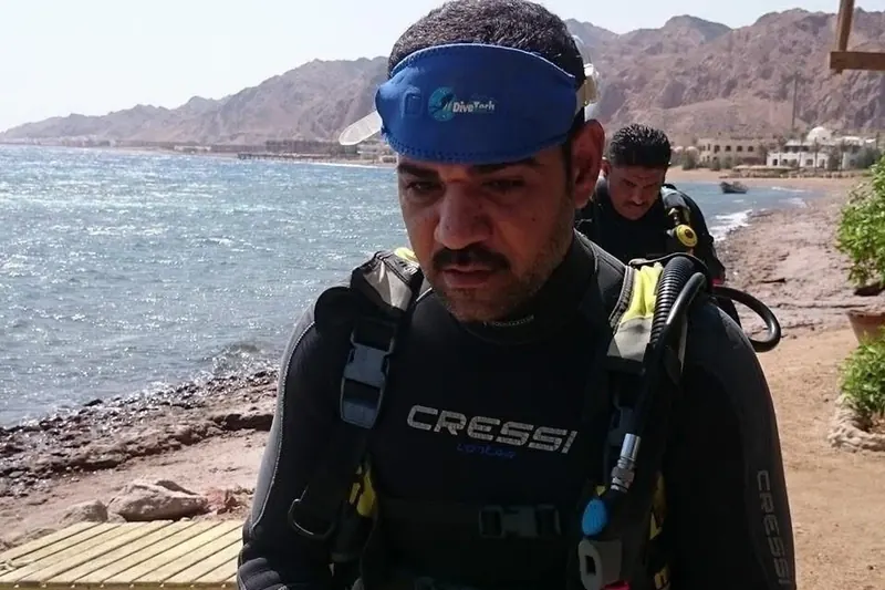 Osama in his wetsuit on the shore before a dive, the Sinai mountains behind him